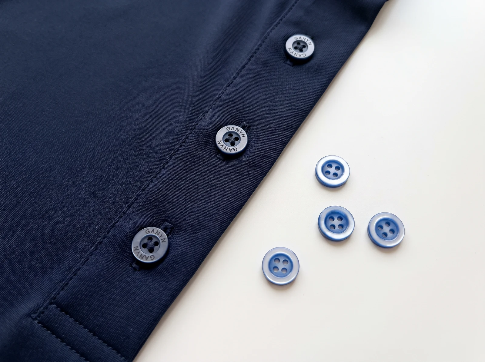 Small polo buttons with laser-engraved GANYN branding on a smooth polyester-elastane placket