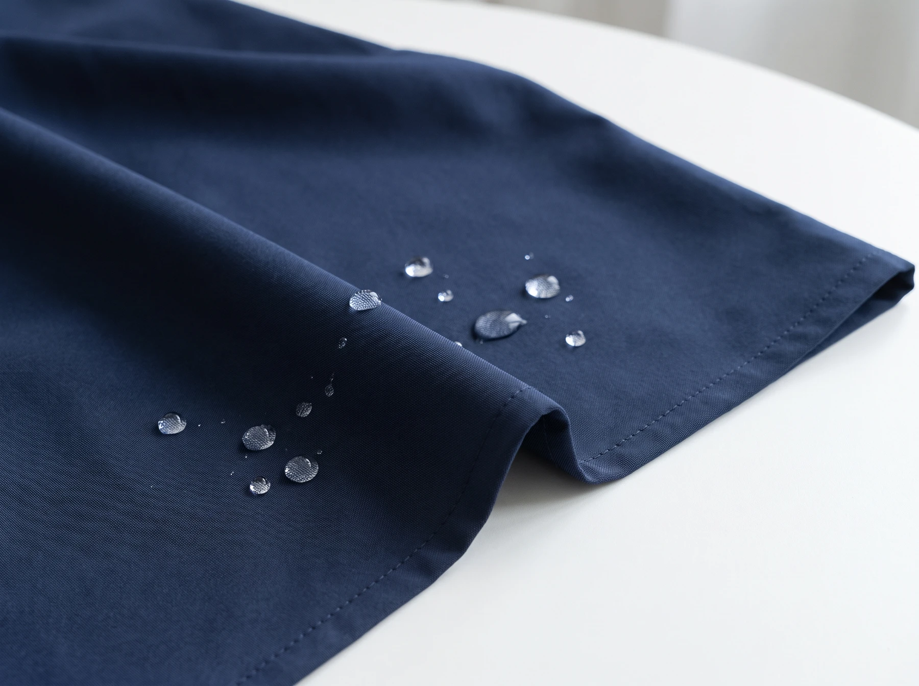 Water droplets beading on a thin fine-woven navy golf windbreaker fabric